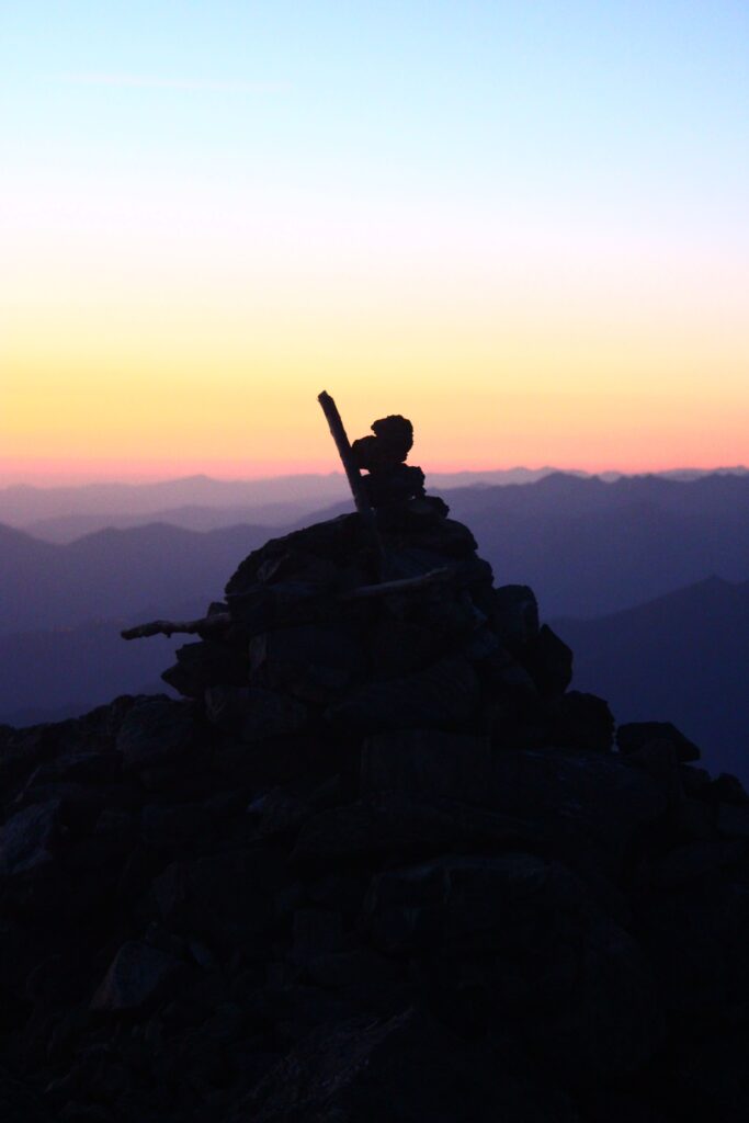 Cairn dans l'ombre face au lever du soleil au sommet du Mont Valier